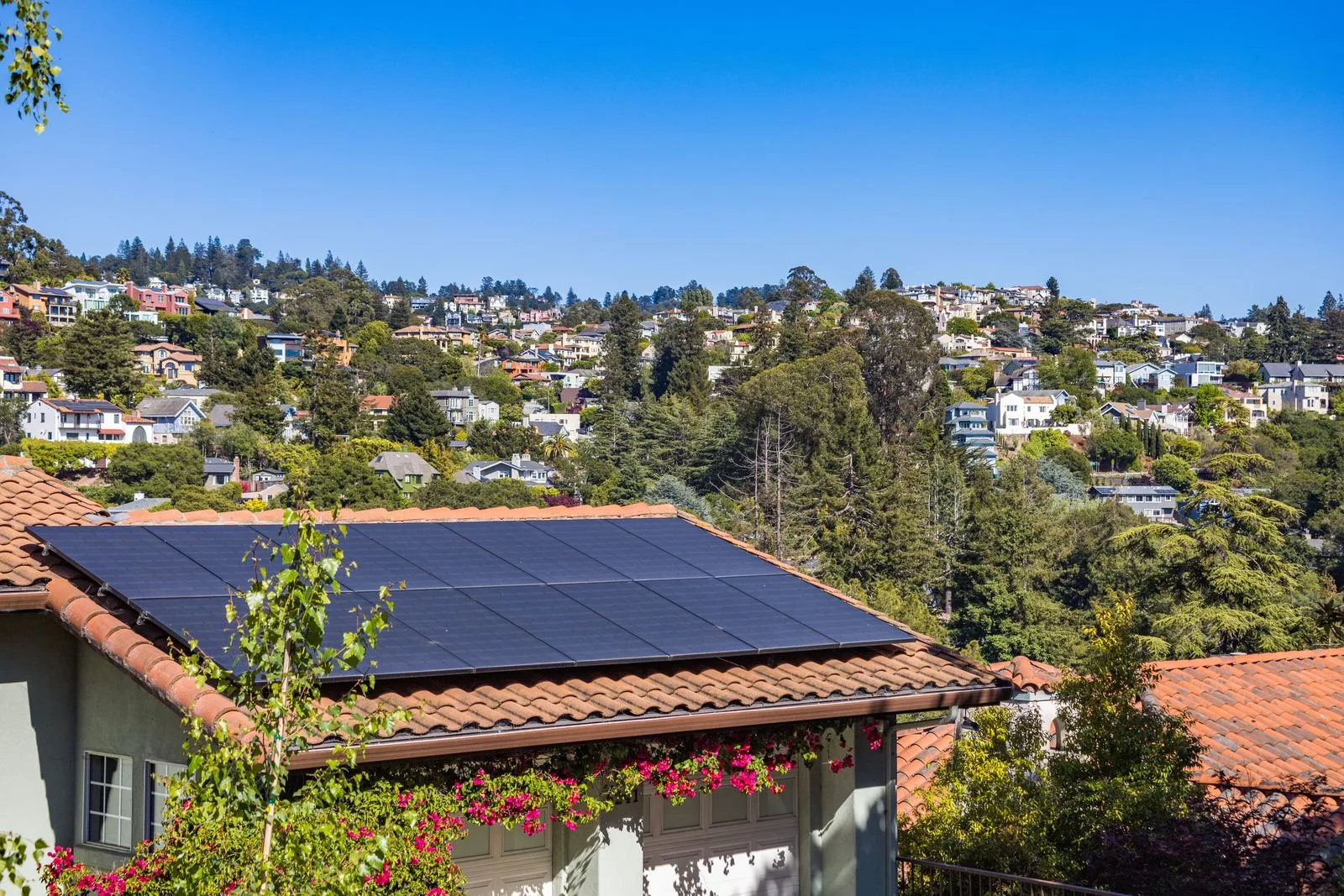 A house with solar panels on its tiled roof, flowers along the wall below