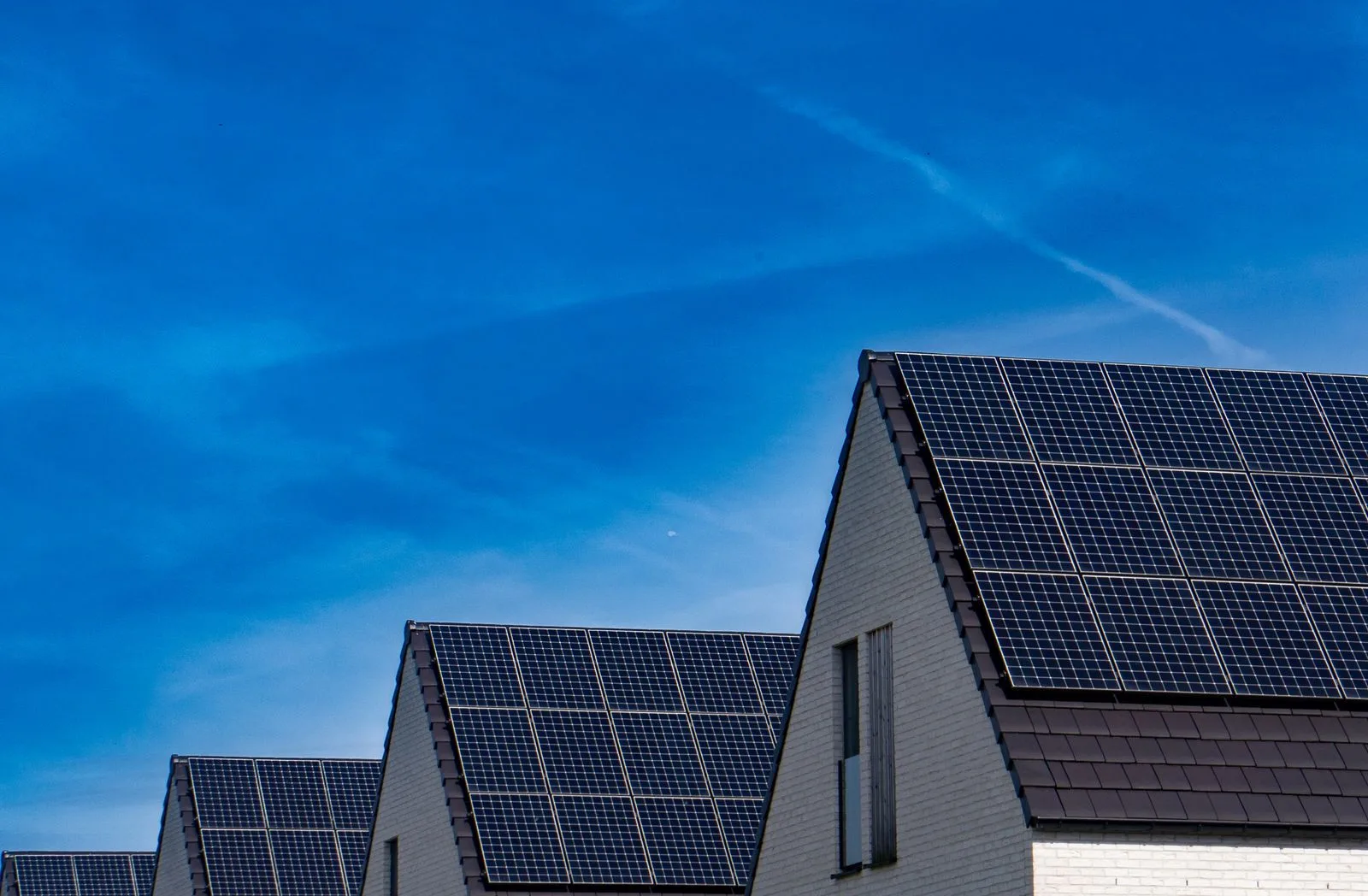 Rows of solar panels on pitched house roofs under a blue sky