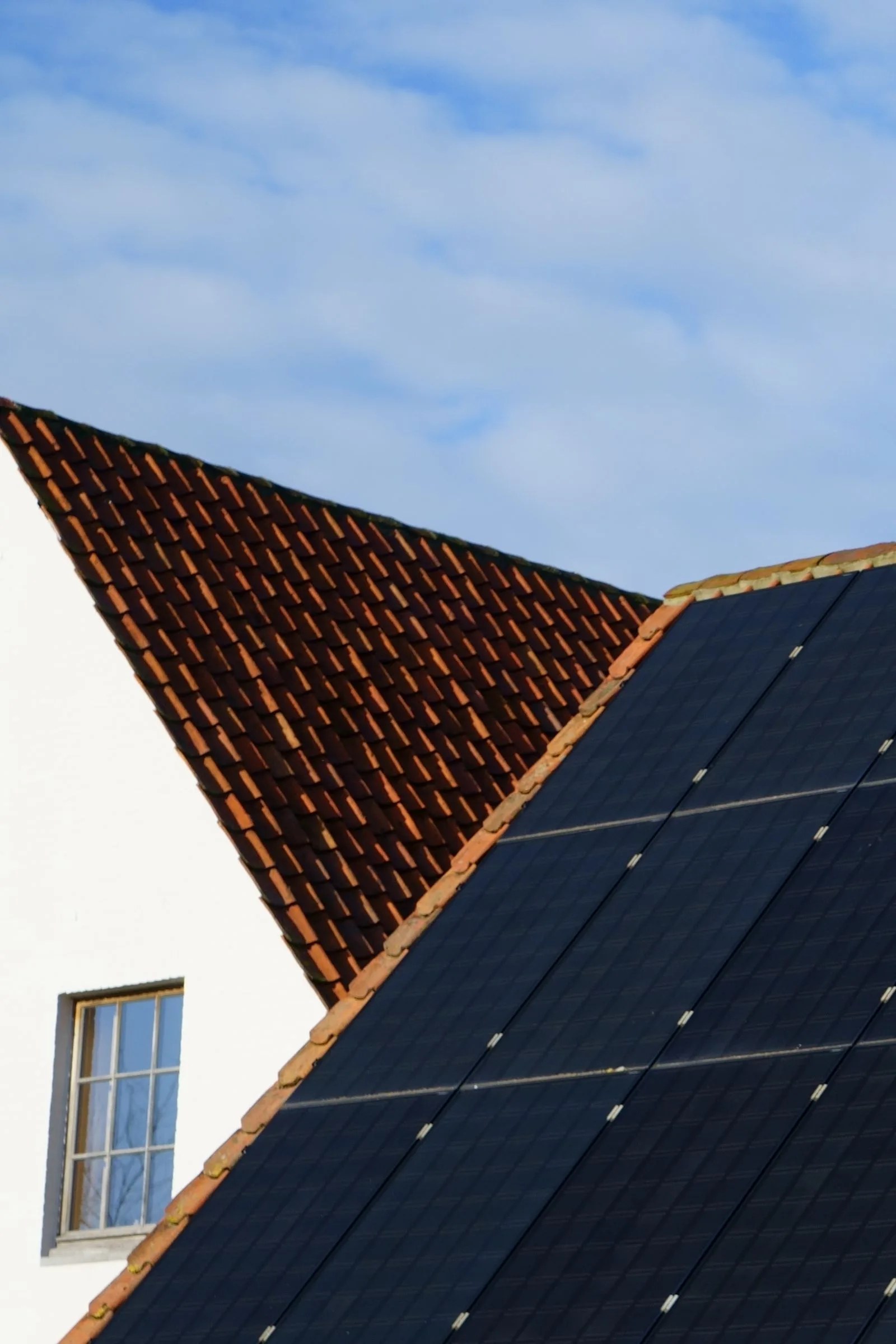 Dark solar panels fitted on a tiled roof beside a white gable wall